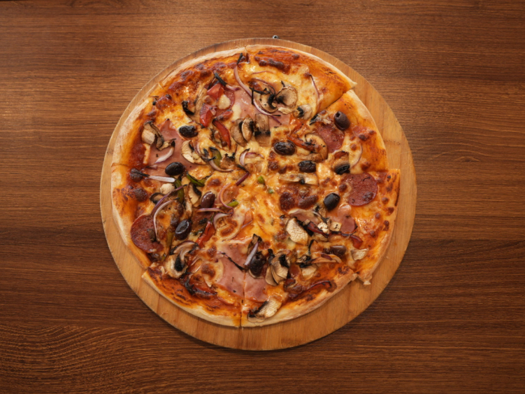 A whole pizza topped with ham, mushroom and olives on a wooden board at Rasa