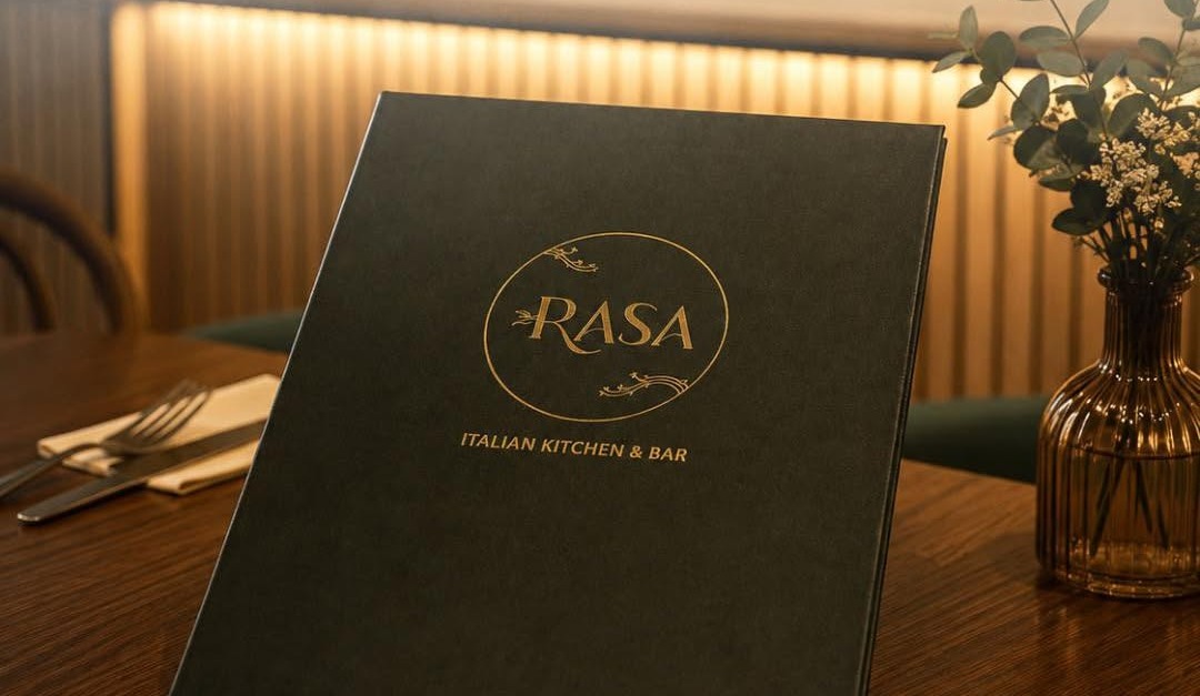 The dark green Rasa menu with its gold logo standing on a set table